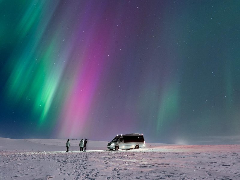 The northern lights over the ice with a vehicle and figures below