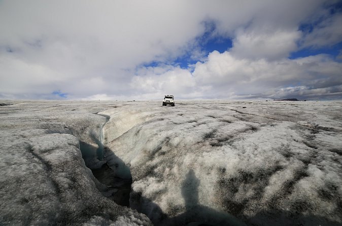 Deep crevasses across the glacier surface with a vehicle on the skyline