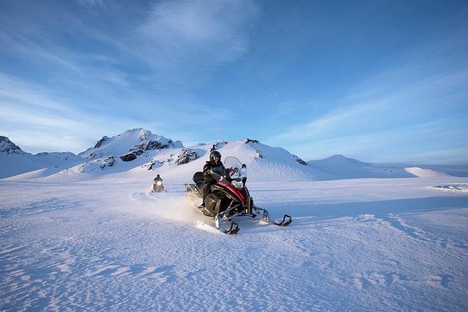 A snowmobile crossing a broad snowfield under a clear sky