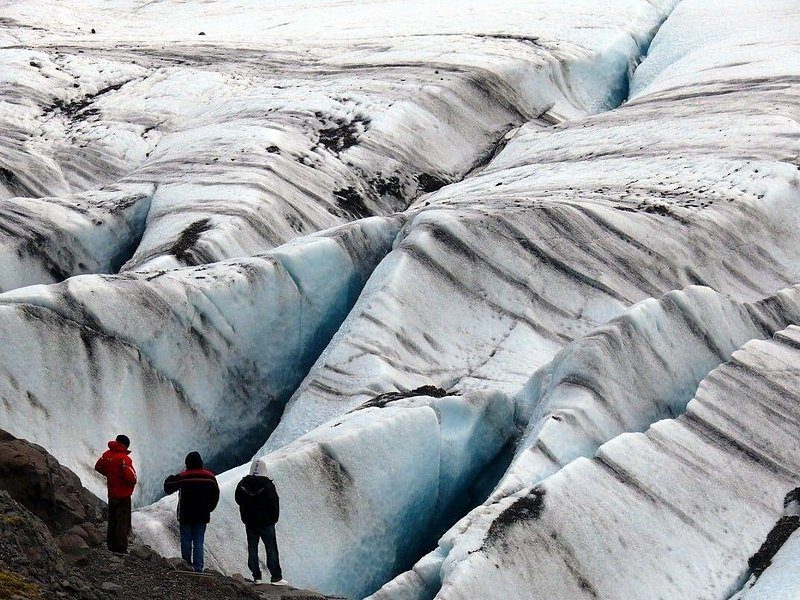 Four small figures walking on the ridged ice of a glacier surface