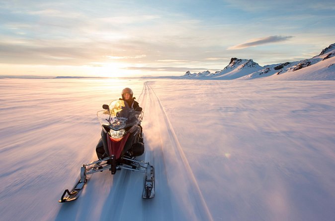 A snowmobile riding towards a low sun over the glacier
