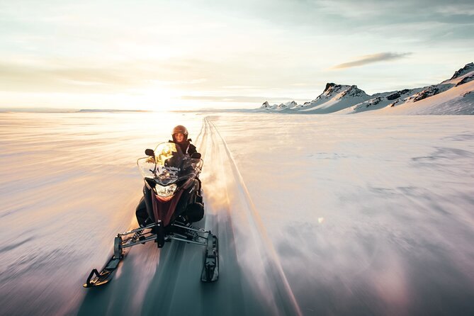 A snowmobile on the ice with the sun sitting low behind it
