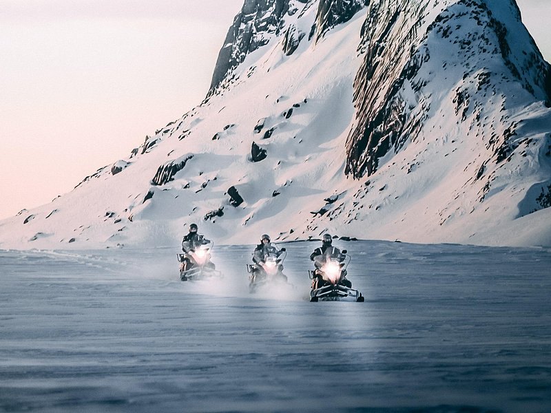 Snowmobiles crossing the ice below snow-covered peaks