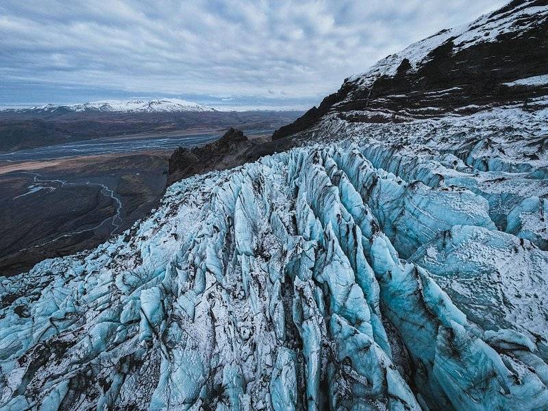 The crevassed snout of a glacier above a braided river valley