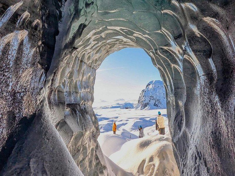 The arched mouth of an ice cave opening onto the snowfield